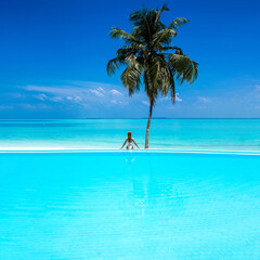 Wall Mural - Elegant tanned woman in white swimsuit in pool on tropical Maldives island. Beautiful bikini body girl in pool with view on horizon. Sexy model near the pool on beautiful Indian ocean landscape.Travel