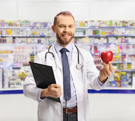 Poster - Young male pharmacist holding a clipboard and a red apple in a pharmacy