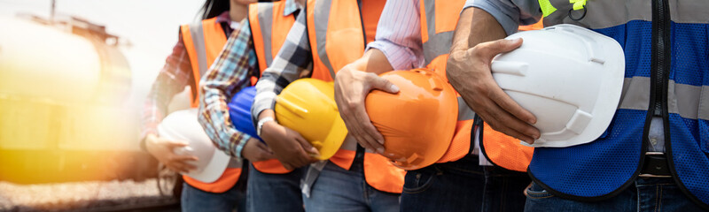 teamwork of diversity engineer holding helmet standing in row on site work at train garage, banner c