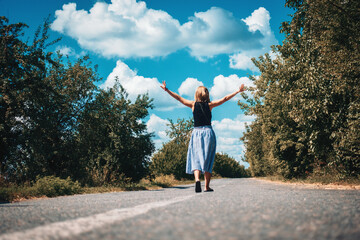 Happy girl walks along the carriageway. Trees grow along the road