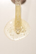 Top view of transparent pipette dropper with light golden drop of serum cosmetics, oil, gel ou cream on beige  background and bubbles of air. Minimal beauty concept, macro closeup with copy space