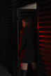 © NASTYA PALEHINA - teen fashion. young girl in black  slim dress-jacket and over the knee boots stands fashion from the back near door frame on black wall background with red studio light. lifestyle concept, free space