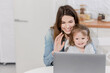 © shunevich - Happy young woman with joyful toddler having video call from relatives, waving hello to them. Beautiful mother with little daughter smiling, using computer to talk online with family while quarantine