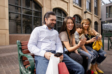 Family Using Smart Phones On City Bench