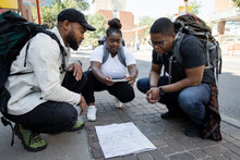 Young Backpacker Friends Looking At Map On Urban Sidewalk