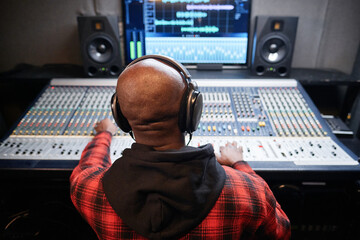 Rear view shot of unrecognizable Black sound engineer producing recording in studio adjusting sound settings