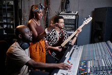 Mature African American Music Producer, Young Female Singer And Male Guitarist Working On Song In Recording Studio