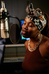 Portrait of modern young African American female singer standing in front of microphone enjoying singing song in recording studio