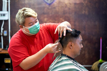 Wall Mural - Barber wearing mask cutting the hair of a client using scissors and comb