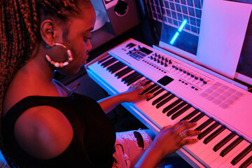 Wall Mural - High angle shot of professional young African American musician playing digital keyboard in recording studio, neon light