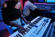 African American Woman Playing Digital Keyboard While Music Producer Working On Mixer In Recording Studio, Neon Lighting