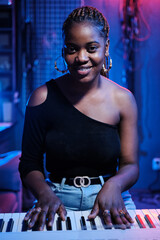 Poster - Vertical medium portrait of young Black woman with digital keyboard in recording studio smiling at camera