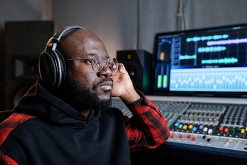 Poster - Serious mature Black music producer wearing headphones attentively listening to audio track thinking about its quality