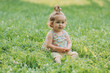 © Tina kids photo - cute little girl with a funny hairstyle is sitting on a blooming green lawn in the park. lifestyle