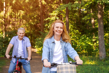 Cheerful active senior couple with bicycle walking through park together. Perfect activities for seniors in retirement lifestyle wearing casual wear smiling happily