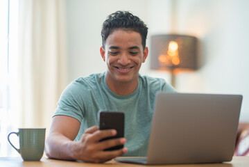 Young black boy using phone and computer connection at home. Happy man reading notification on mobile cellular while work on laptop in smart working. Modern Z generation people using web