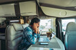 Leinwandbild Motiv Adult man sitting at the desk using laptop computer and mobile phone connection to work in alternative office inside a camper van. Smart working digital nomad concept people lifestyle