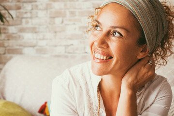 Wall Mural - Portrait of cheerful adult woman smiling and enjoying life at home sitting on the sofa. Excited expression female people looking on her side. Attractive young lady enjoying leisure with a smile