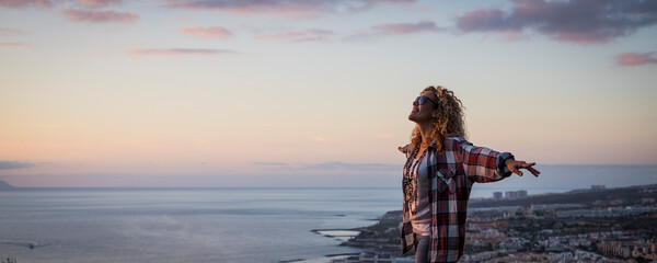 Happy woman outstretching arms with sunset on the ocean coast in background. Concept of joy and freedom life for female people. Independence and travel leisure activity. One person enjoying life