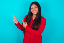 Young Latin Woman Wearing Red Shirt Over Blue Background Points At Copy Space Indicates For Advertising Gives Right Direction