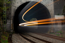 Fast Train Coming To Light Out Of A Tunnel With Old Concrete Portal Near Altena Germany In Rural Lenne Valley. Long Time Exposure Shows Motion Of Passenger Train In A Curve With Traces Of Head Lights.