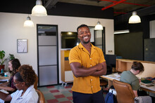 A Black Business Owner Stands With His Arms Crossed While Creative Team Works