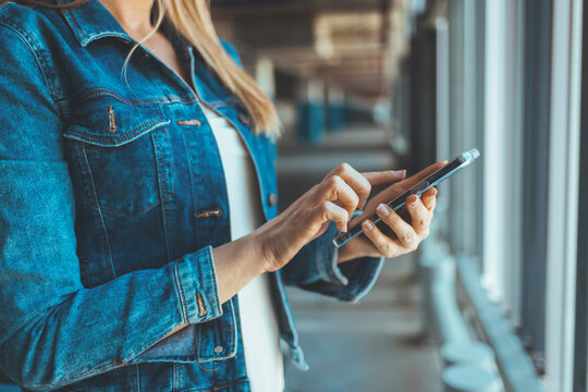 A young Caucasian woman standing nearby car texting message on a smartphone. Attractive brunette with long hair using mobile phone chatting or surfing the internet on the roadside.