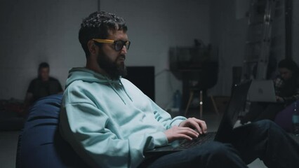 Close view of programmers typing on a laptop keyboard and working in a bomb shelter hearing missile strikes and explosions during the war