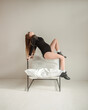 pregnancy fashion. young pregnant girl in black bodysuit sits fashion in profile on the white cubic modern chair near white wall background and looks up in sag. lifestyle pregnant concept, free space