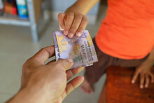 Close-up Of Man Giving Rupiah Banknotes To Little Girl