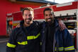 © Halfpoint - Happy firefighters crew with fire station and truck in background looking at camera.