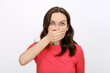 portrait of stunned shocked brunette woman in red T-shirt with her hand over mouth on white background, news