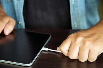 Man's hand unplugging a tablet charger on a wooden table in the wrong way