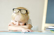 Little child wearing glasses is having fun with a book. Cute boy is watching pictures and learning letters. Preparation for school, early childhood development. Activities in kindergarten