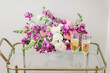 purple and white flower arrangement with champagne glasses on bar cart