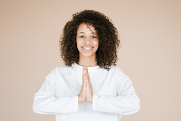 Wall Mural - Joyful happy african american young woman joined hands, thanking for good luck, isolated on brown studio background. Girl smiling female prayer waiting for miracle                               