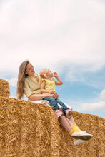 Mother And Child Are Having Fun On The Farm. Mother And Fair-haired Daughter Are Sitting On Haystack In The Field
