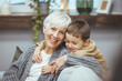 © Dragana Gordic - Grandma and grandson spend time together watching a funny video or cartoon on the phone, laughing while grandson hugs her. They enjoy their modern home.