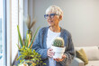 © Dragana Gordic - Caring for potted plants. Beautiful mature woman at home in casual clothes.  Woman Caring for House Plant. Woman Taking Care of Plants at Her Home Portrait of Elderly Woman Gardening at Home.