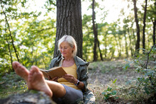 Senior Woman Relaxing And Reading Book Outdoors In Forest.