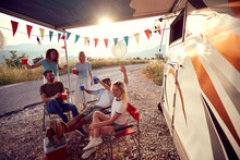 Young Friends Cheering And Celebrating In Front Of Camper Rv Outdoors In Nature. Summertime Holiday In Nature, Vanlife. Togetherness, Travel, Lifestyle, Holiday Concept.