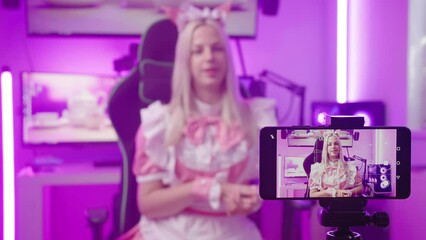 Wall Mural - Cute blonde maid influencer in pink cyberspace recording video with smartphone 4K