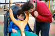 A disabled boy and his father enjoy playing in the park playground with a special needs swing.