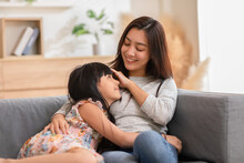 Close Up Of A Proud Mother Watching Her Baby Snuggling On Her Chest While Their Both Sitting At A Sofa In The Living Room. An Innocent Asian Kid Is Cute And Sending Smile To Mom At Home