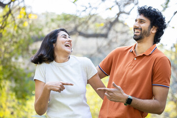 Happy indian couple laughing in the park, cheerful urban man and woman wearing casual t-shirt having fun together, friendship.