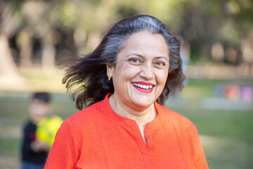 Portrait of happy Indian asian grey-haired senior woman standing in the park copy space. Smiling old retired female.