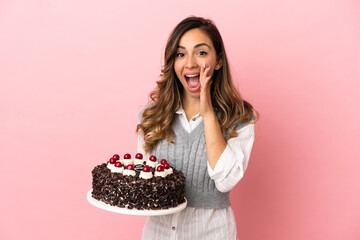 Wall Mural - Young woman holding birthday cake over isolated pink background with surprise and shocked facial expression