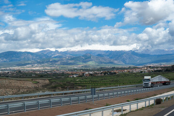 Wall Mural - Special transport truck with a large concrete beam driving along the highway and with the Sierra Nevada in the background covered by clouds.