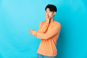 Wall Mural - Young Chinese man isolated on blue background with surprise expression while pointing side