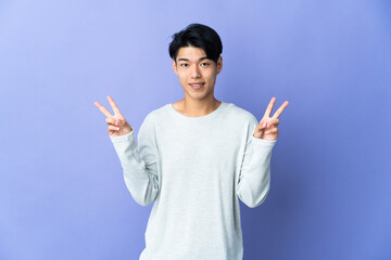 Wall Mural - Young Chinese man isolated on purple background showing victory sign with both hands